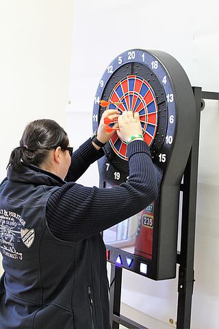 Bildtext: Dartspielerin beim Herausnehmen der Wurfpfeile.