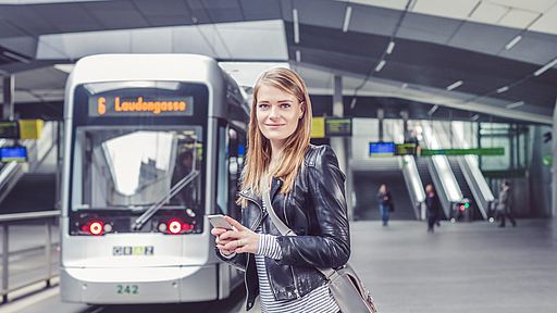 Bildtext: Junge Dame mit Mobiltelefon bei Haltestelle